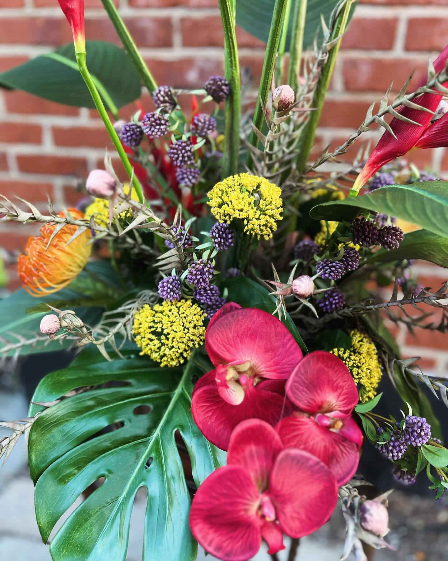 Tropical arrangement with red orchids, heliconia and monstera leaves